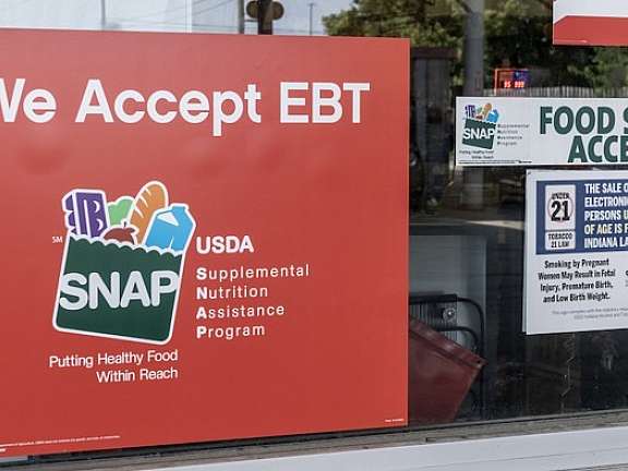 A storefront window displays signs that read We Accept EBT and Food Stamps Accepted, indicating that SNAP benefits are accepted at this location. Other notices and payment options like GPay are also visible.