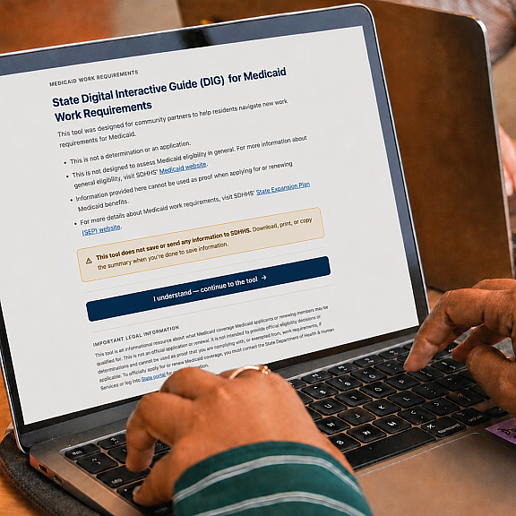 Person using a laptop displaying a webpage titled State Digital Interactive Guide (DIG) for Medicaid Work Requirements, with highlighted warnings and a blue button to continue. Colorful sticky notes and another laptop are nearby.