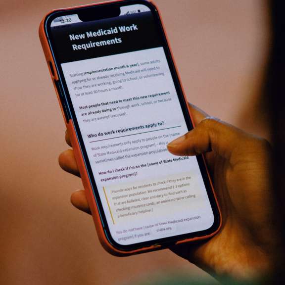 A person holding a smartphone with a screen displaying information about new Medicaid work requirements, including questions and details in black and white text.