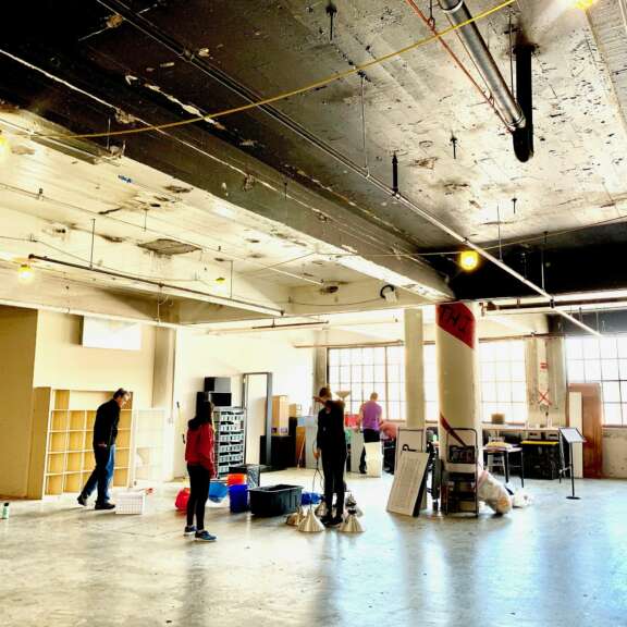 People in a large room with a white pillar and people standing around.